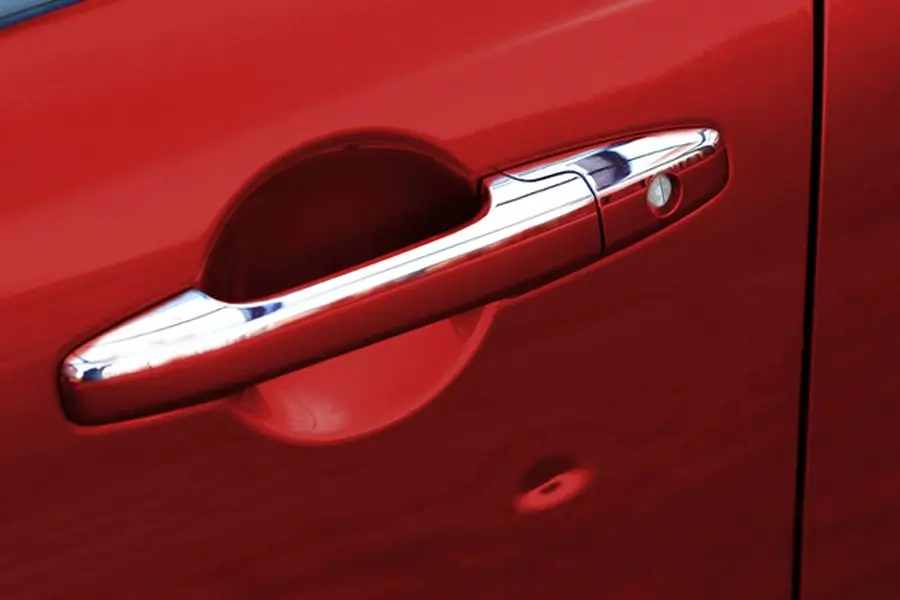 A shiny chrome car door handle with a keyhole, on a bright red car body
