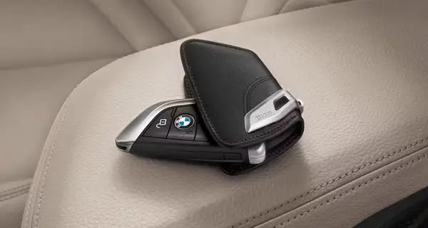 A black and silver BMW car key partially enclosed in an open black leather key case, resting on a beige car seat.